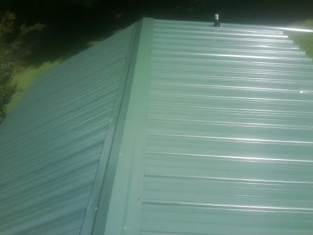 New green metal panels meeting at the ridge of a roof — Flat Roof Repair work by our crew in Slidell