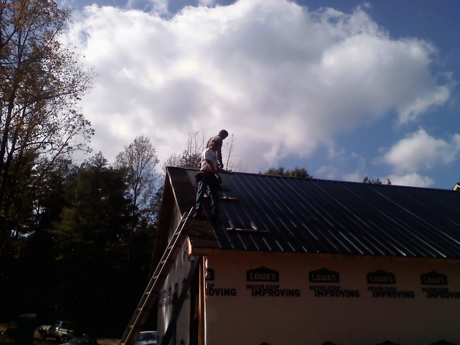 Roofer fastening dark metal panels high against a cloudy sky, from a Roof Inspection job in Slidell