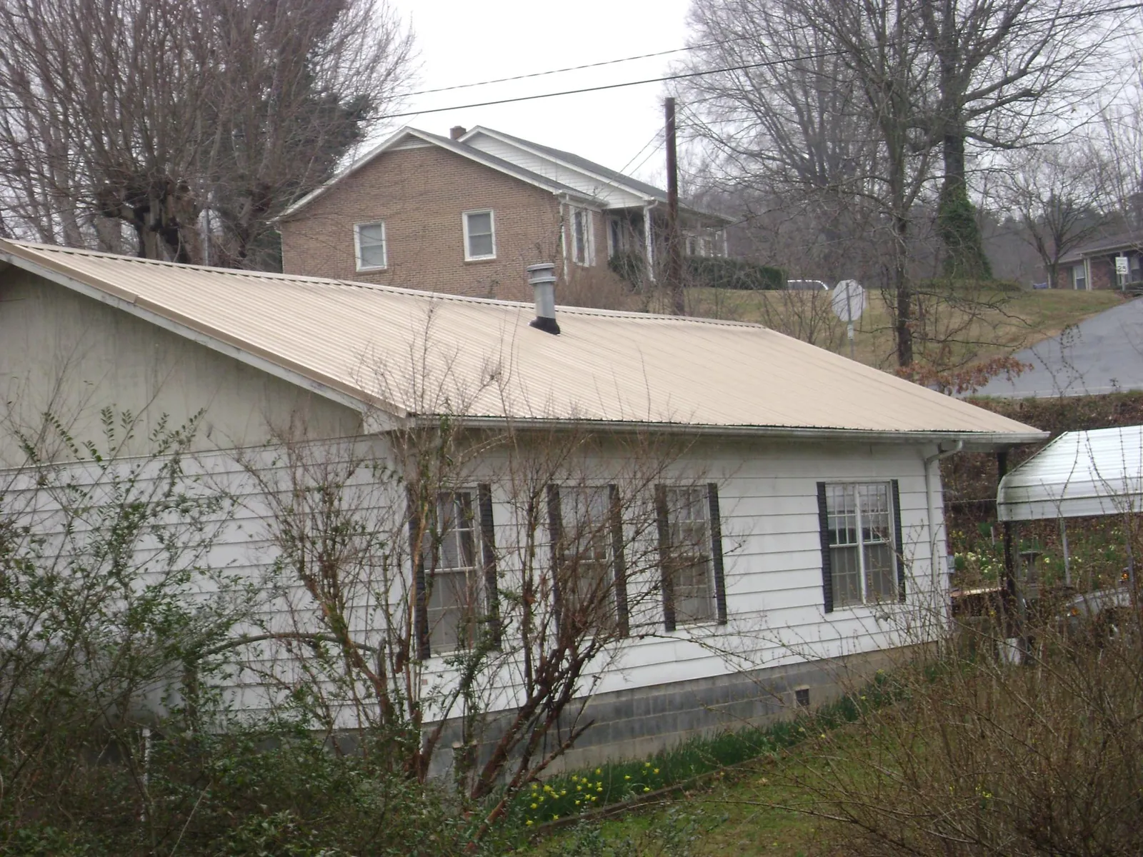 Tan metal roof on a white sided house set into a hillside — Commercial Roofing by Roofing Brothers in Slidell
