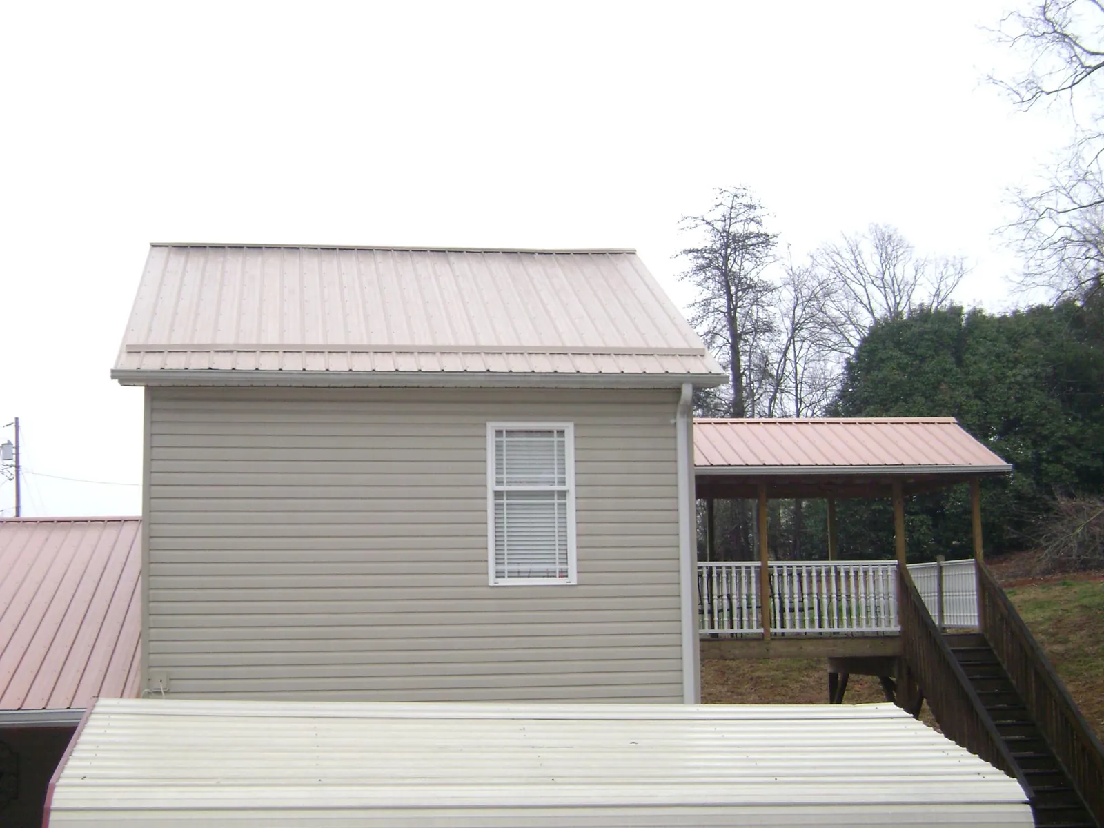 Tan metal roofs on a two story addition and attached porch, from a Roof Replacement job in Slidell
